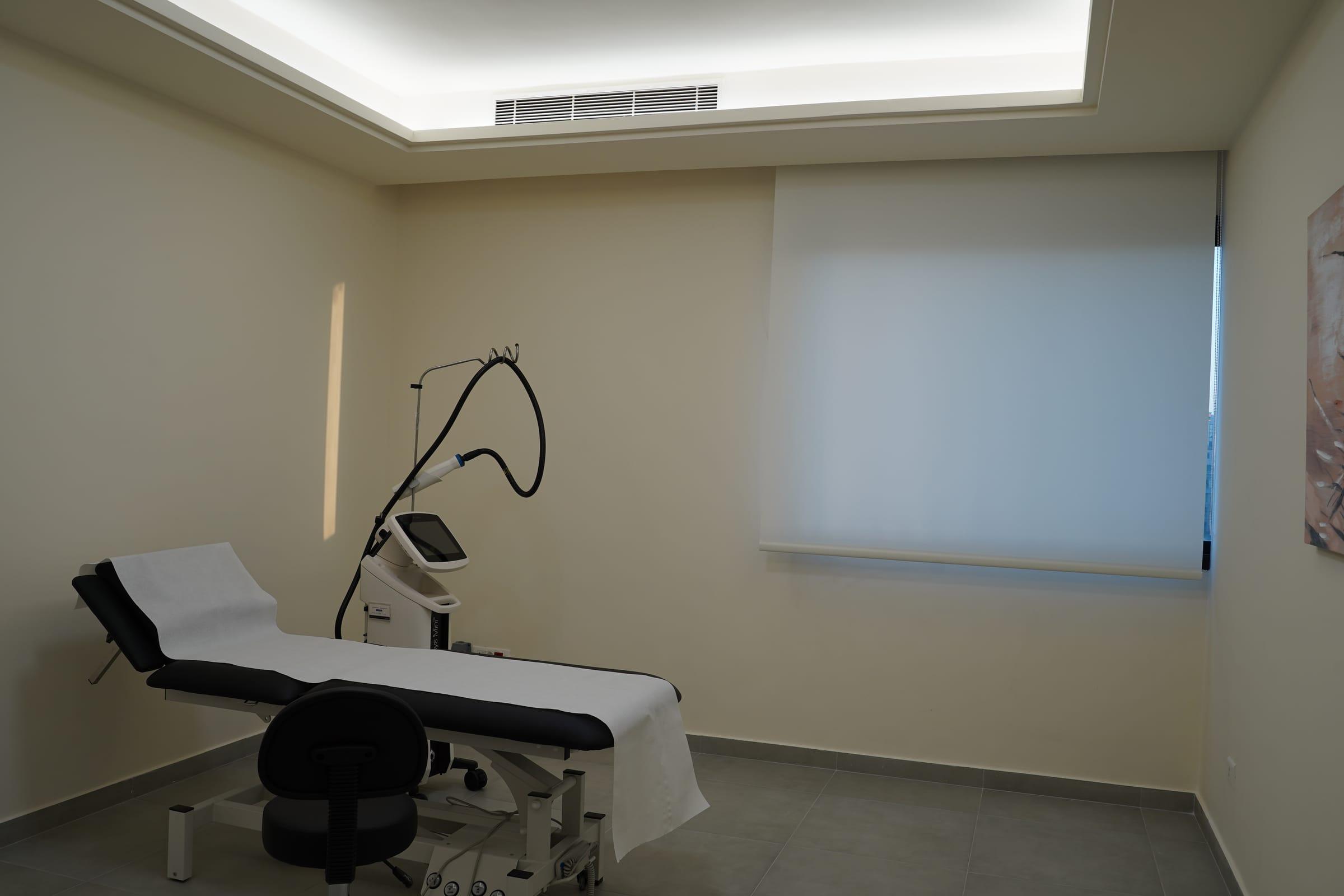 Treatment room with a laser device and treatment bed at Le Dermato